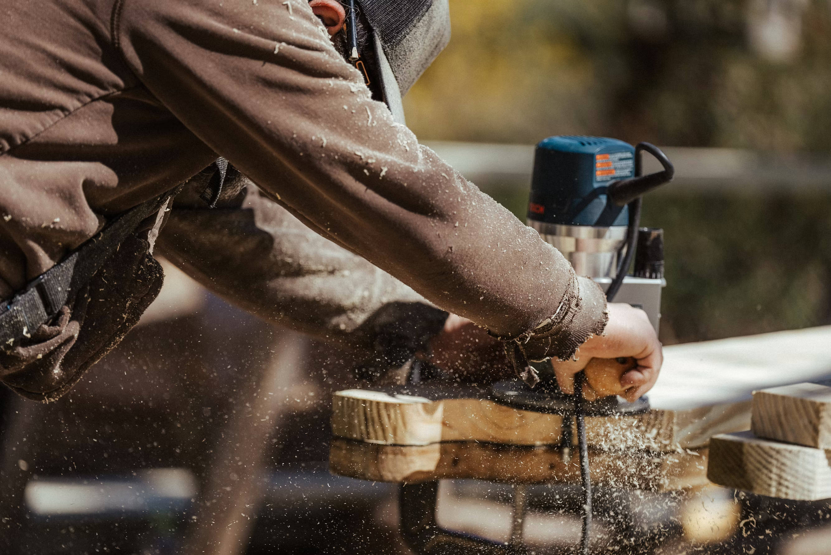Worker using power drill on wooden beam with sawdust flying