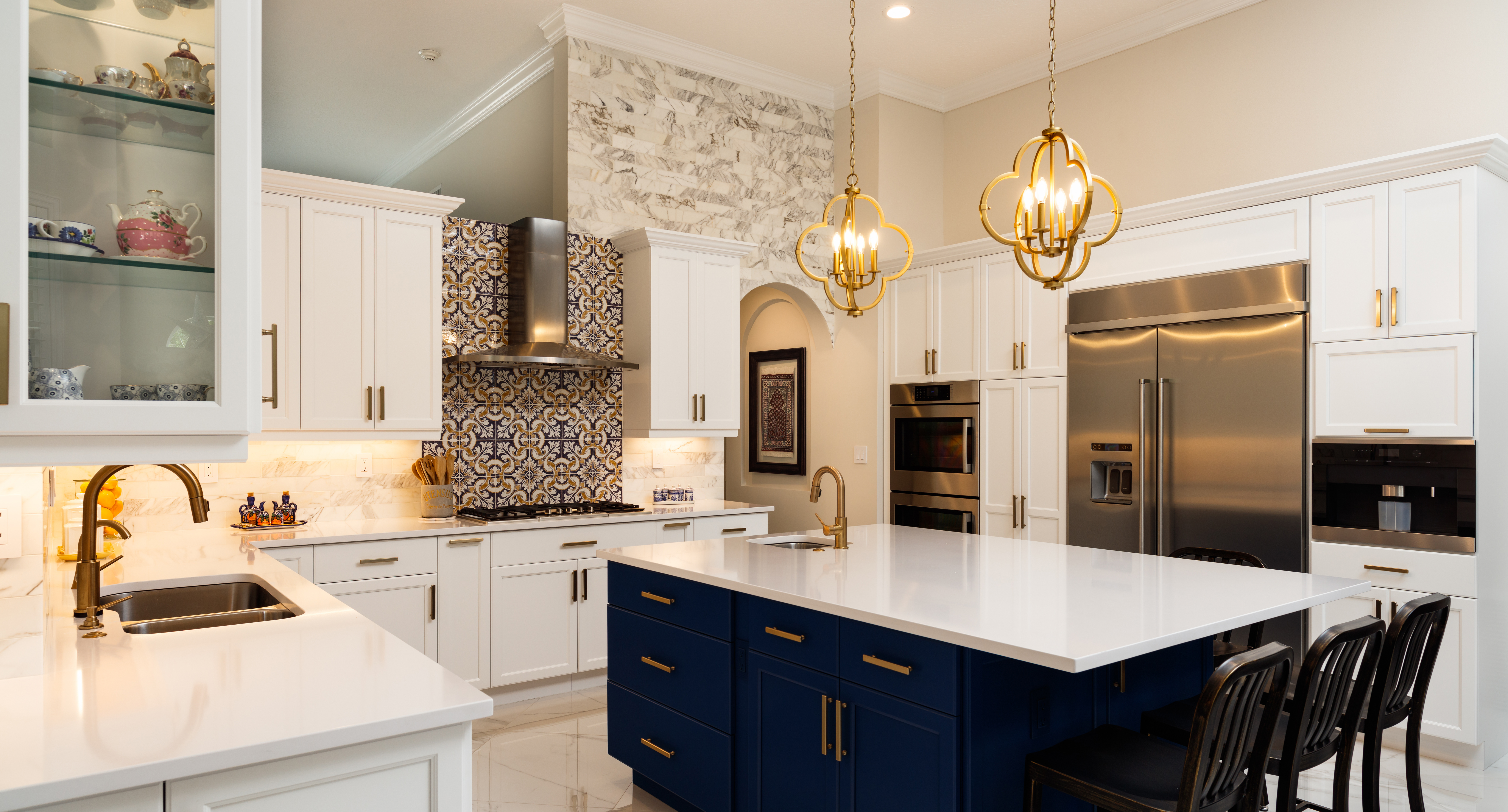Modern kitchen with white cabinetry, blue island, stainless steel appliances, and gold pendant lights