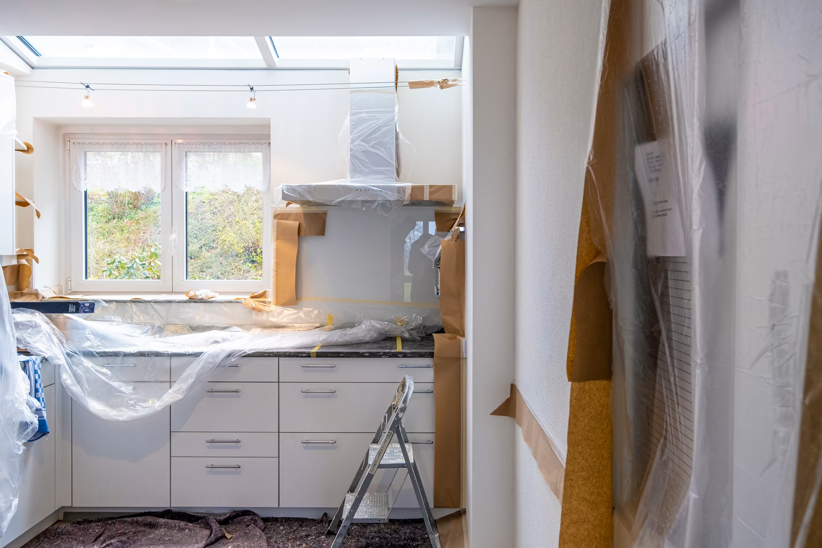 Kitchen renovation in progress with protective plastic covering countertops and appliances