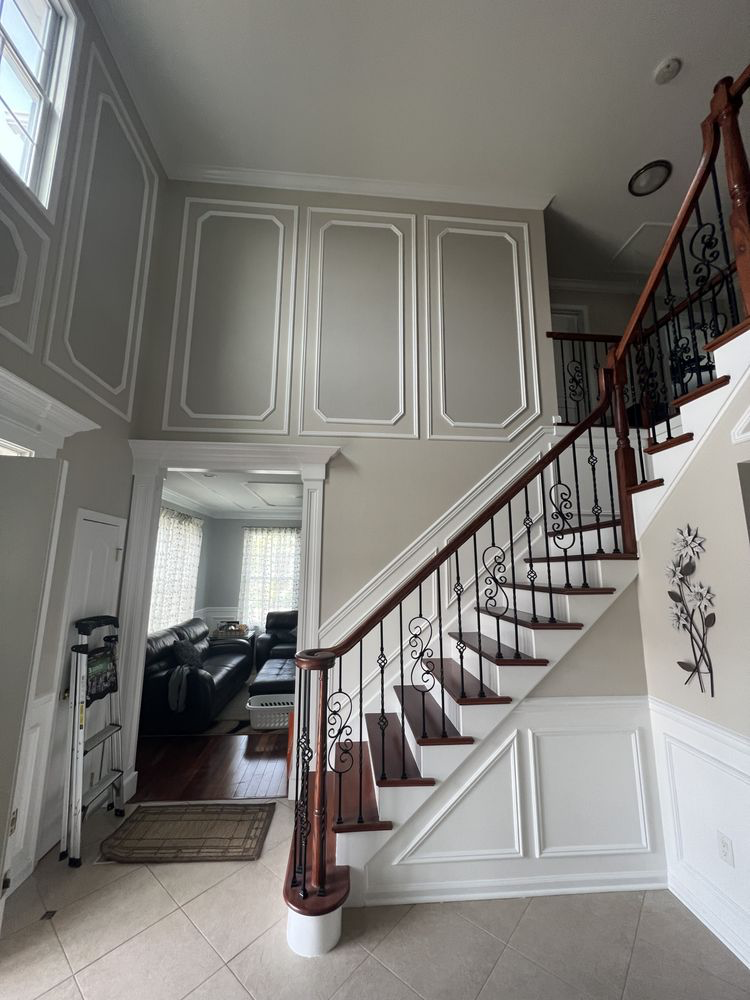 Elegant foyer with grand staircase, ornate railings, high ceilings, and decorative wall panels