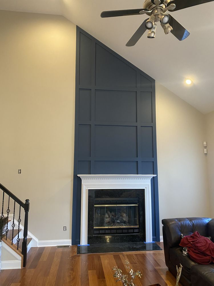 Modern fireplace with dark blue paneled wall surround, white trim, and black marble hearth in open living room