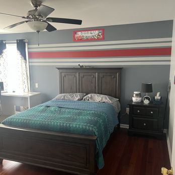Modern bedroom with dark wood bed, teal bedding, striped accent wall, ceiling fan, and nightstand