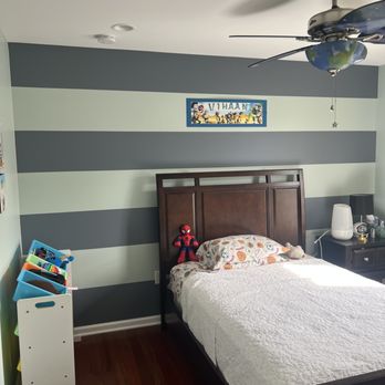 Child's bedroom with striped gray and white walls, wooden bed frame, and ceiling fan